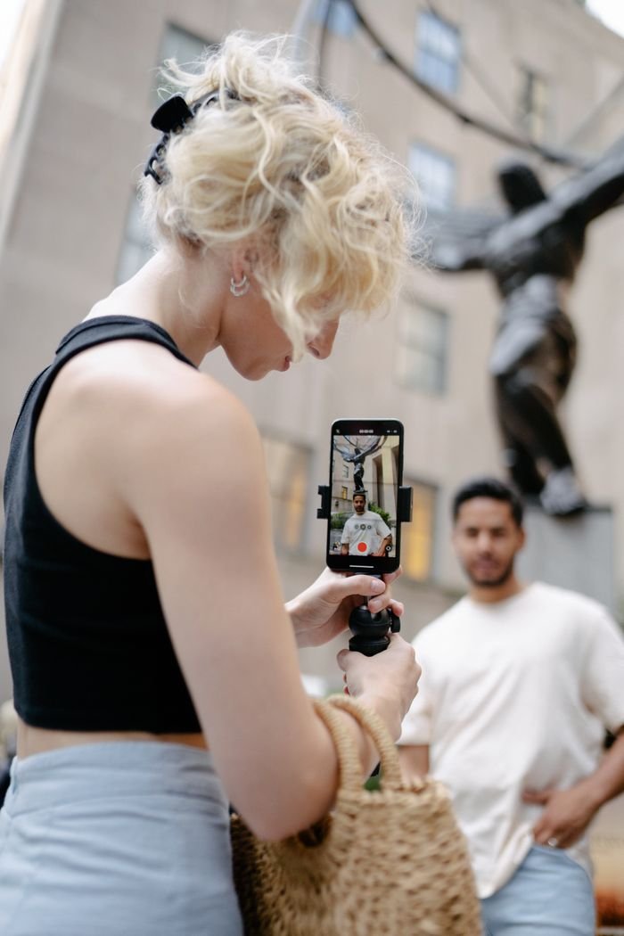 A young woman records a man in an urban setting using a smartphone.