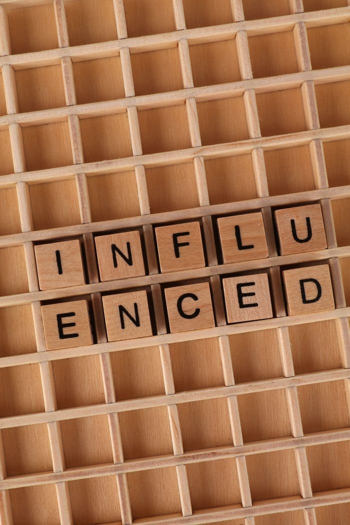 Close-up of wooden Scrabble tiles spelling 'influenced' on a grid.