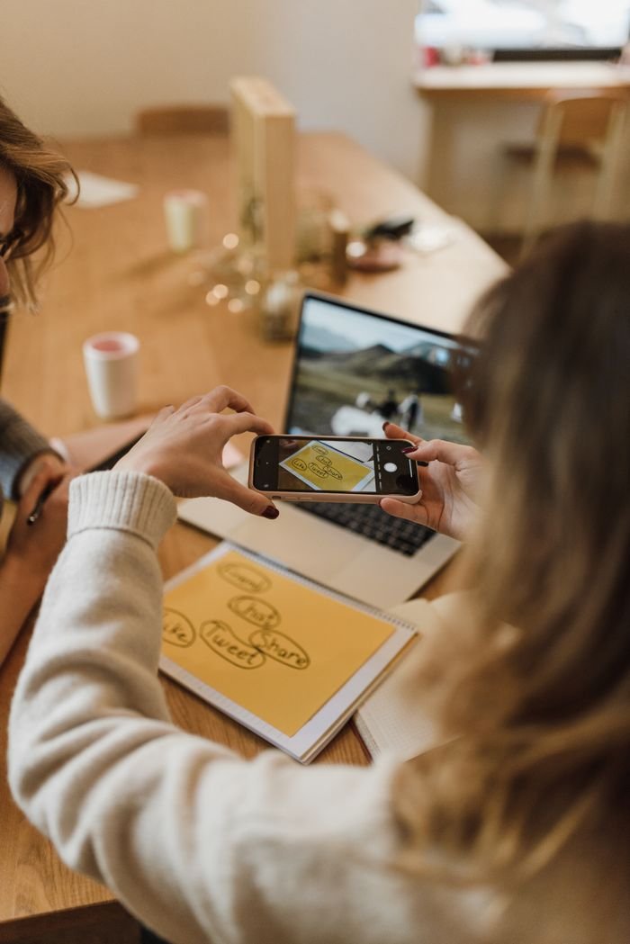 A woman uses her smartphone to take pictures of notes during office work, illustrating modern technology use.